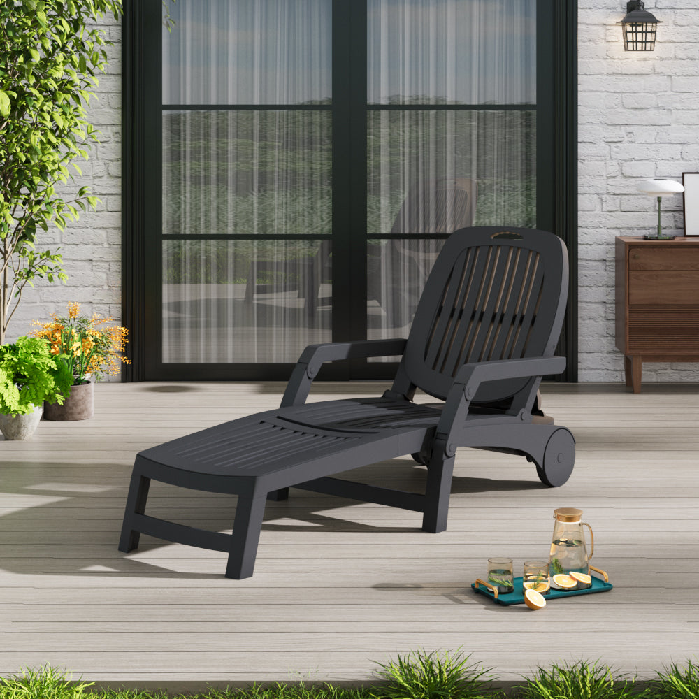 Black garden lounge chair on wooden patio with green plants background