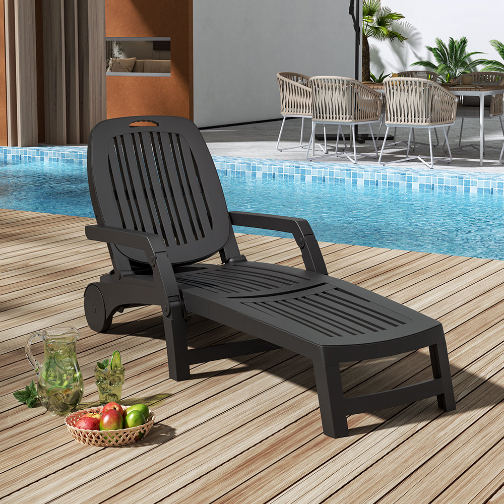 Black reclining chair beside pool with towel and cold drink